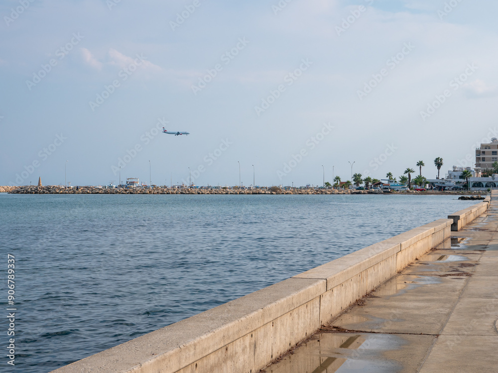 Airplane preparing to land at the airport of Larnaca, Cyprus. Flying low above calm smooth blue mediterranean sea with rocky wave breaker and promenade.