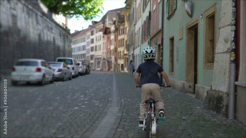 Naklejka premium Boy cycling through scenic cobblestone street lined, historic buildings, emphasizing adventure and exploration in a quaint urban setting, ideal for travel