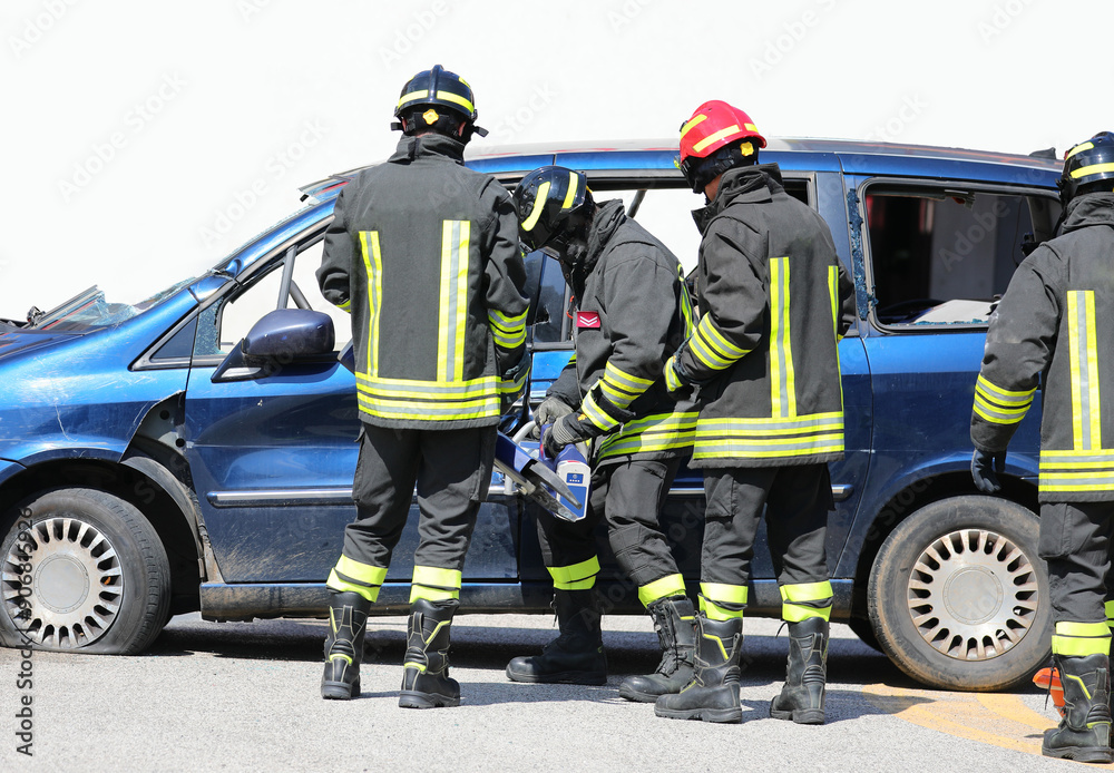 Fototapeta premium Firefighters using shears and hydraulic spreaders pry open the doors of the crashed car after road accident