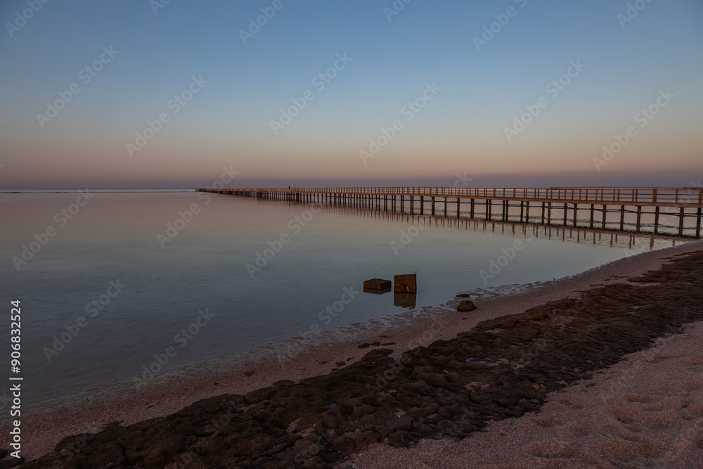 Fototapeta premium Long pier near the sea. Beautiful summer evening. Smooth water with reflection.