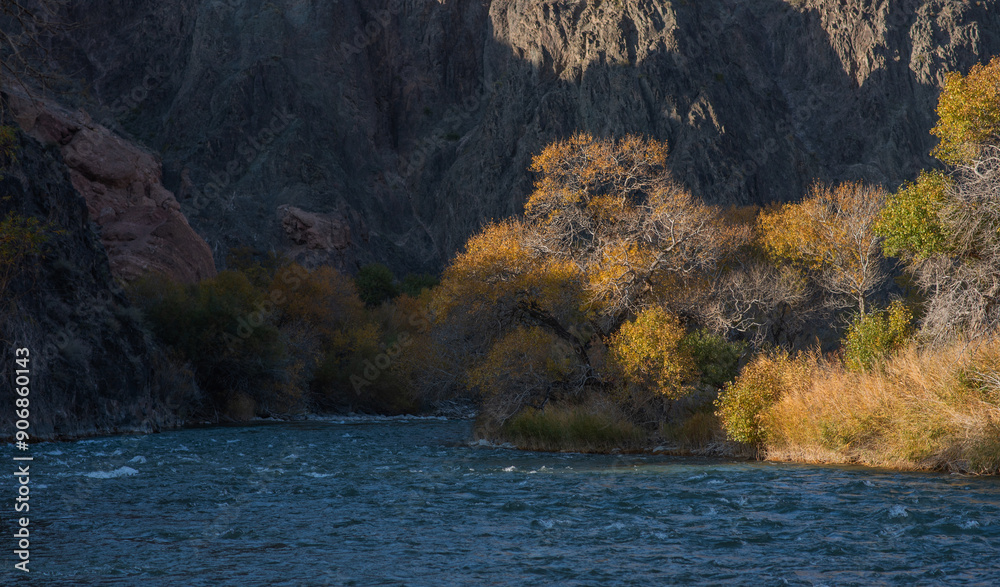 Amber foliage frames a mountains river, meandering at the foot of towering, rugged cliffs under the gentle embrace of a clear azure sky. Amber foliage frames a mountains river, meandering at the foot of towering, rugged cliffs under the gentle embrace of a clear azure sky.