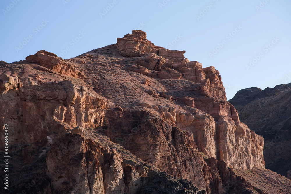 Fototapeta premium The rugged beauty of a desert landscape is captured as the sun casts its glow on sandstone spires, which stand proudly against a clear, pale sky.