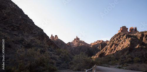 a tranquil desert landscape bathed in soft light, featuring distinctive rock formations against a clear blue sky, with sparse vegetation dotting the rugged terrain, situated in the American Southwest photo