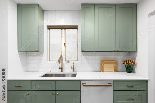 A kitchen detail with sage green cabinets, white marble countertop, square tile backsplash, and a gold faucet.