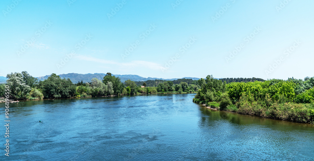 Overlooking a serene river, the foreground showcases a rustic terracotta-tiled roof, with lush greenery on the banks and distant mountains under a clear expansive sky. Overlooking a serene river, the foreground showcases a rustic terracotta-tiled roof, with lush greenery on the banks and distant mountains under a clear expansive sky.
