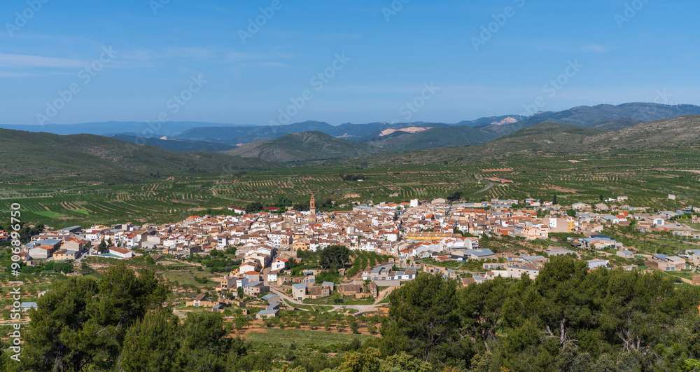 panoramic view of a traditional Spanish town with clustered houses and a church spire, amid vast green landscapes and rolling hills under a clear sky. panoramic view of a traditional Spanish town with clustered houses and a church spire, amid vast green landscapes and rolling hills under a clear sky.