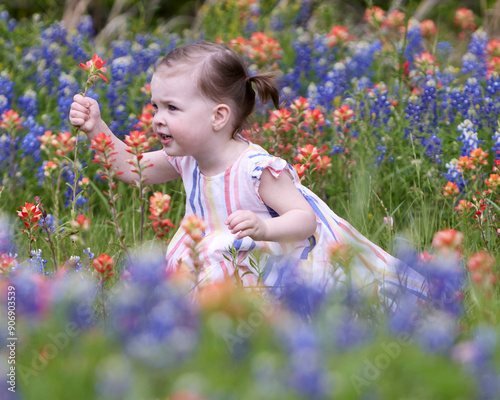 A pretty little girl in a striped sundress, squats in field of wildflowers, holding up her newly picked flower. photo