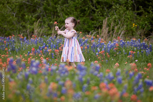Enthusiastic about the flower she just picked, a little girl stands in a spring meadow of  orange, red, and blue wildflowers.