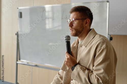 Side view portrait of adult male professor in glasses giving lecture on law speaking in handheld microphone in university classroom, copy space photo