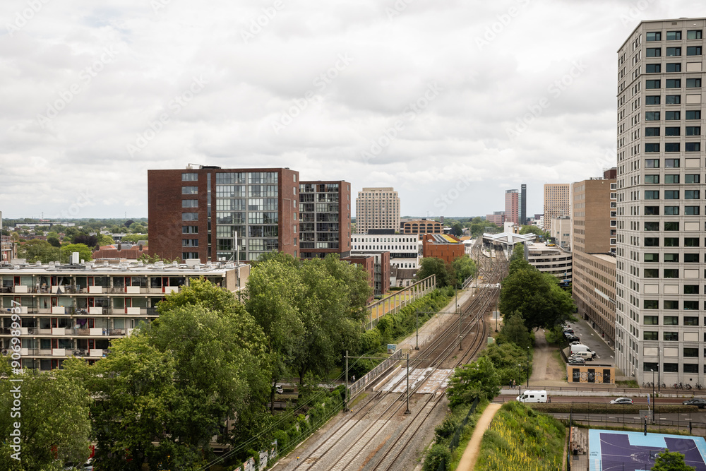 Fototapeta premium Spoorpark rail park and train track near rooftop view of Dutch city Tilburg in the Netherlands. Apartment blocks and skyrises next to train station in Holland under cloudy sky on grey day