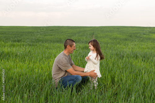 a little girl with long hair with her father in a field of green wheat. young wheat. father and daughter