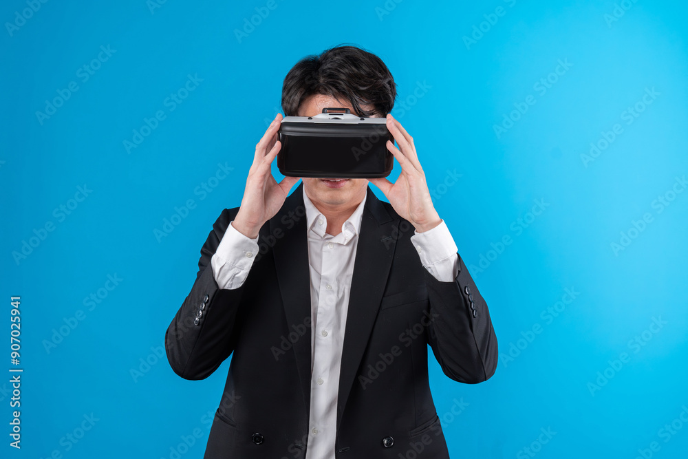 Smiling Asian businessman looking thorough VR connecting to business world report in futuristic metaverse, analyzing innovation technology ads in virtual reality isolated blue copyspace. Contrivance.