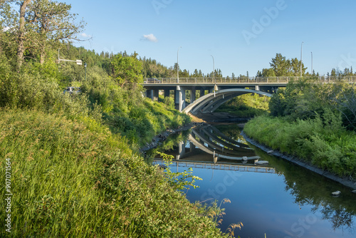 Fox Drive bridge crosing whitemud creek in day light with blue sky background and reflection in calm creek water photo