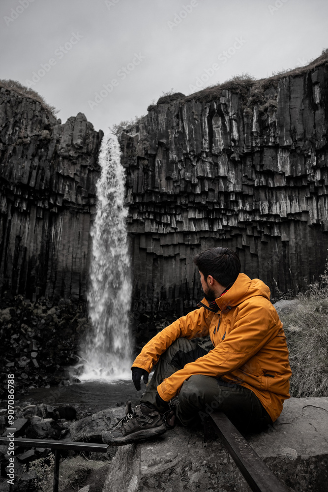 young latin guy sitting on the rocks looking at a waterfall