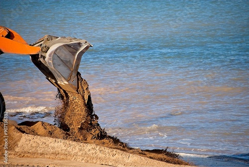 A bulldozer pushes sand to redraw the beach for erosion control.