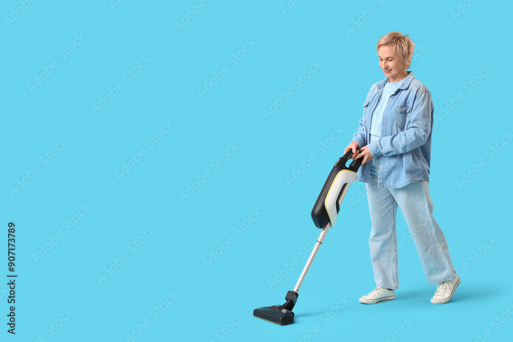 Mature woman using vacuum cleaner on blue background Mature woman using vacuum cleaner on blue background