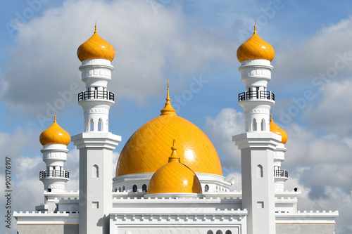 Facade of a white mosque with yellow domes and minaret tops photo