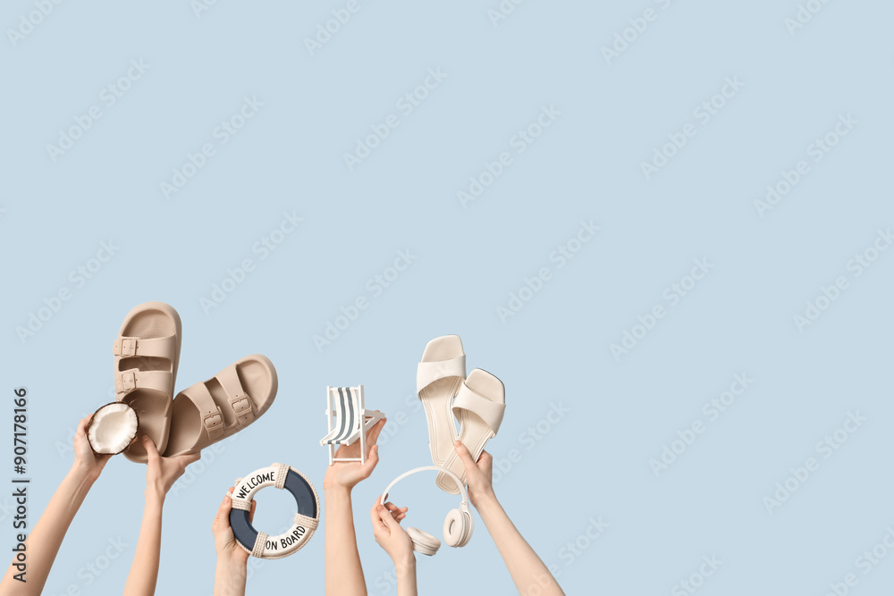 Fototapeta premium Hands holding flip flops with headphones, tiny deck chair, coconut and decorative lifebuoy on blue background