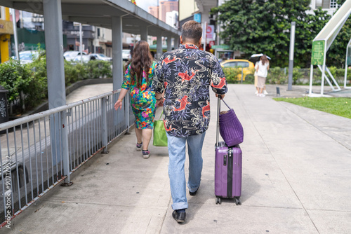 Photography 50-something Malay man and 30-something Chinese woman in colorful clothes walking together with suitcases near a train station in Kuala Lumpur, Malaysia