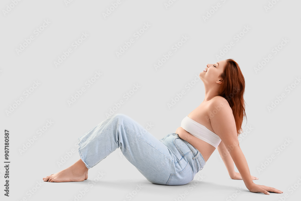 Young plus size woman sitting on light background