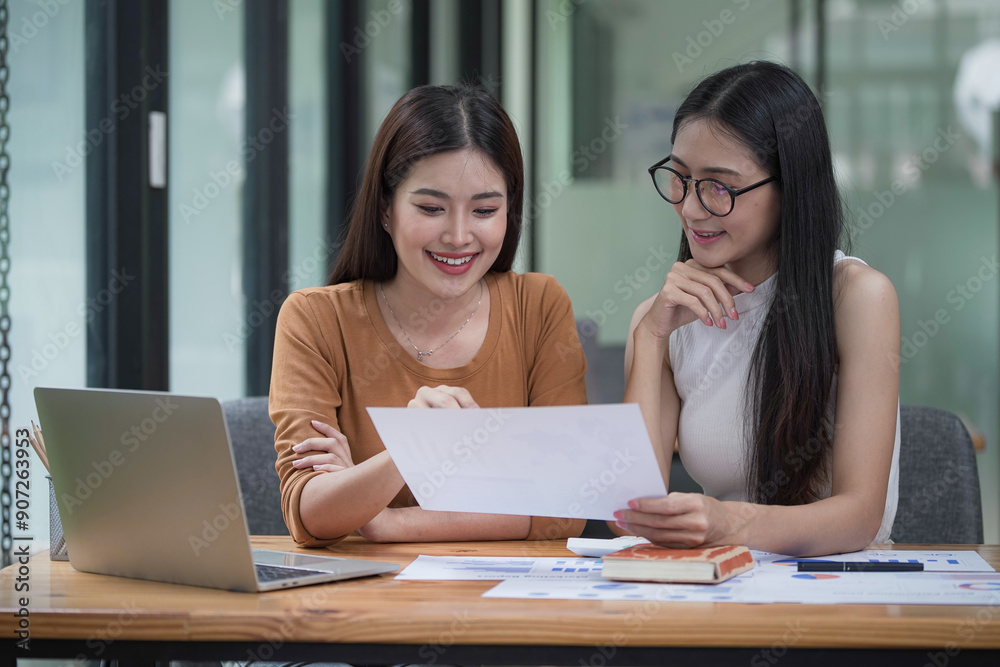 Two young Asian businesswomen discussed investment project work and planning strategy. Business people talk together on laptop computers at the office. Two young Asian businesswomen discussed investment project work and planning strategy. Business people talk together on laptop computers at the office.
