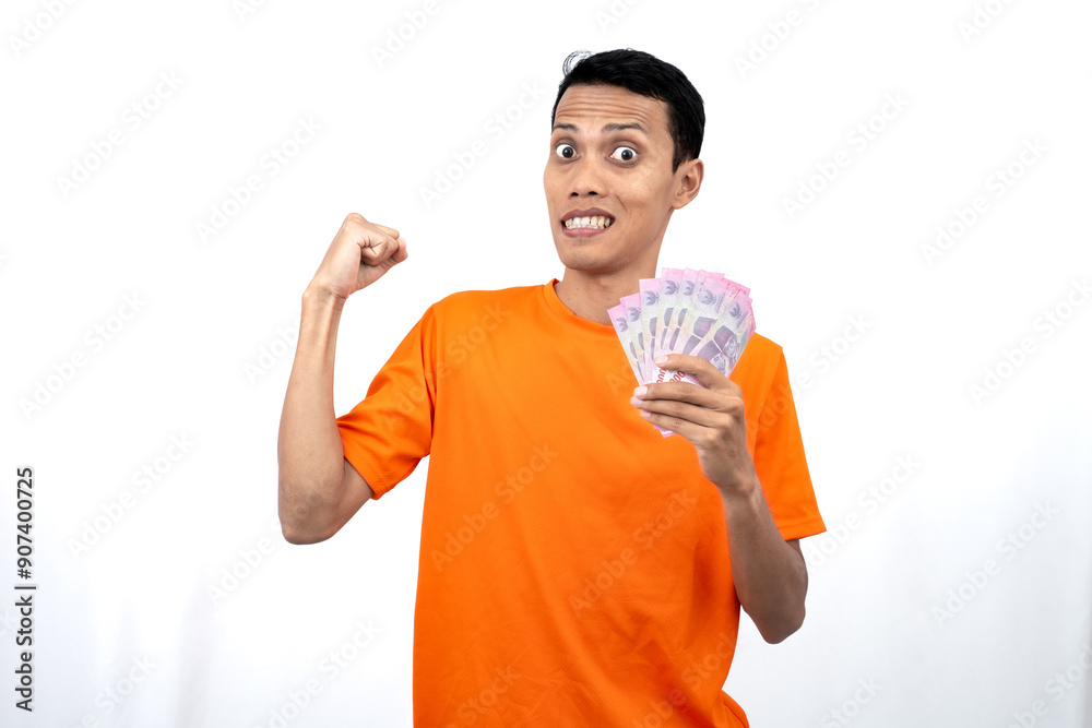 Portrait of a young Asian man wearing an orange t-shirt with a happy, surprised, pleased expression while carrying hundreds of thousands of rupiah. isolated on a white background. Portrait of a young Asian man wearing an orange t-shirt with a happy, surprised, pleased expression while carrying hundreds of thousands of rupiah. isolated on a white background.