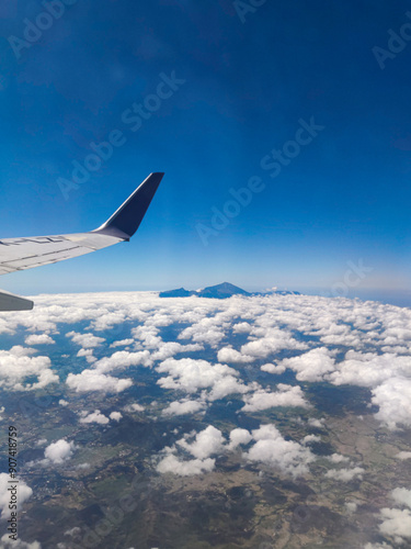 view of blue sky and clouds from an airplane window, wing of airplane, view from airplane window, landscape of mountain outside of airplane window, airplane window view over java island photo