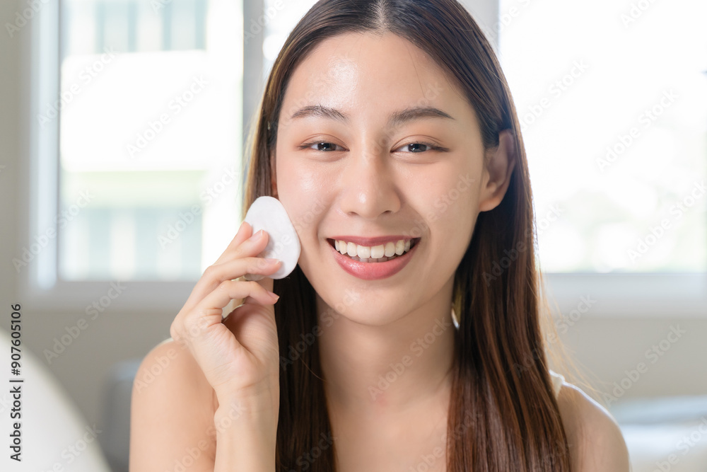 Happy asian woman looking at mirror and using cotton pad clean make up on her face Happy asian woman looking at mirror and using cotton pad clean make up on her face