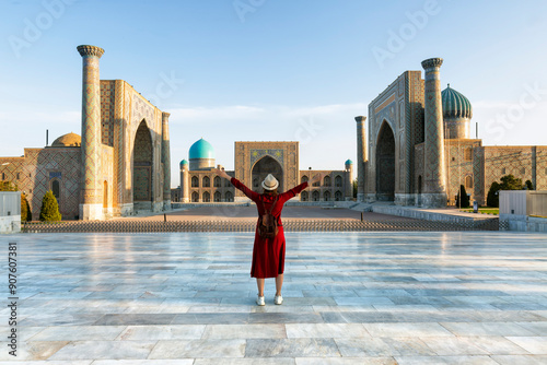 Uzbekistan, Samarcanda - young girl standing with open arms looking Registan square. Translation: In the name of Allah Almighty who creates