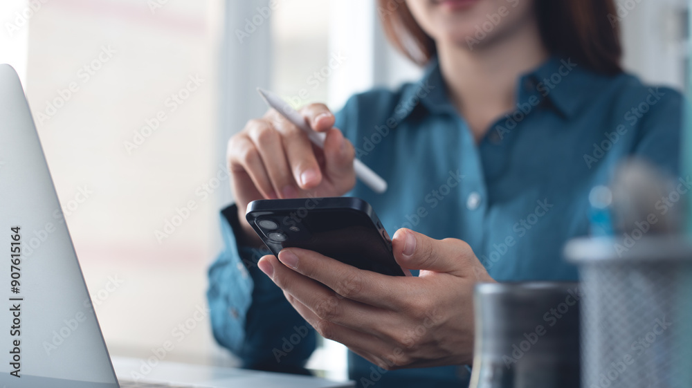 Businesswoman using mobile smart phone during working on laptop computer at office. Asian woman using smartphone searching the information, surfing the internet with laptop on office table