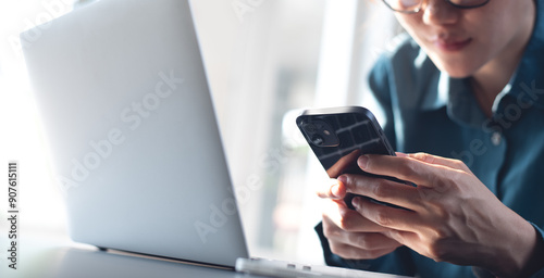 Asian business woman using mobile phone, surfing the internet during working on laptop computer at modern office. 