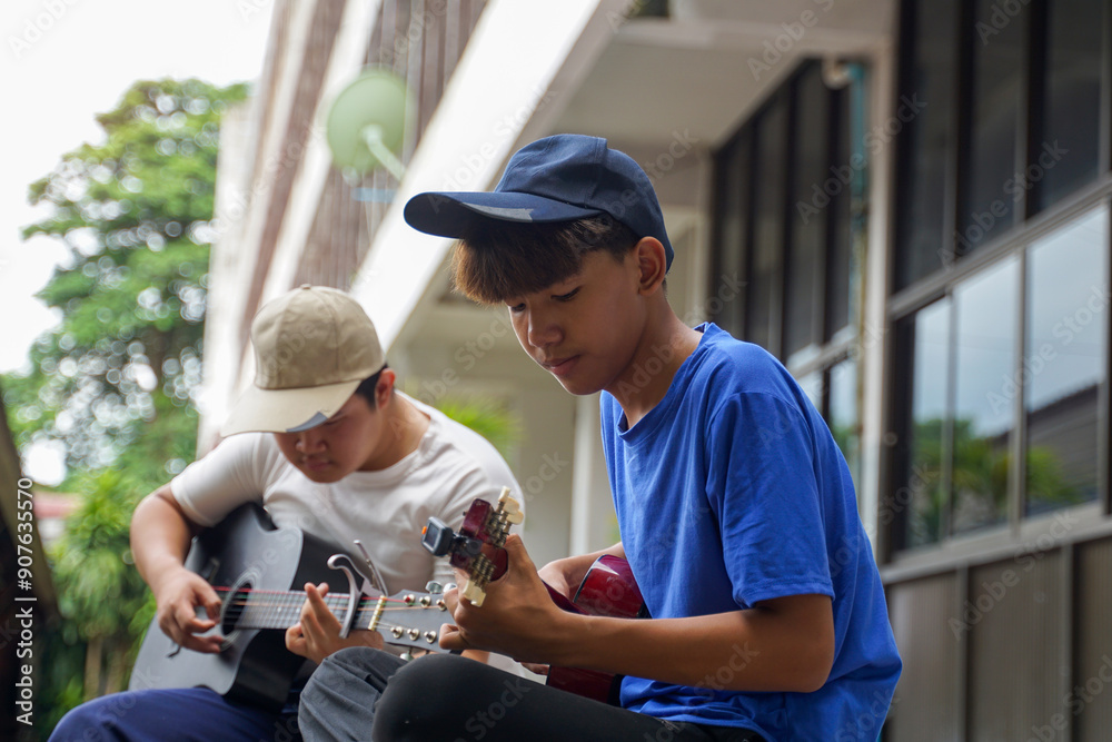 Fototapeta premium Young Asian male playing ukulele with friends during break from school. They are happy and relaxed. Concept of teenagers, friends, leisure activities.