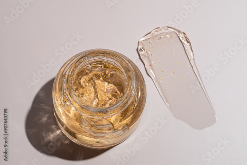 top view of glass jar and a smear of 24k gold cream gel for skin care on beige background. Luxury cosmetics presentation. photo