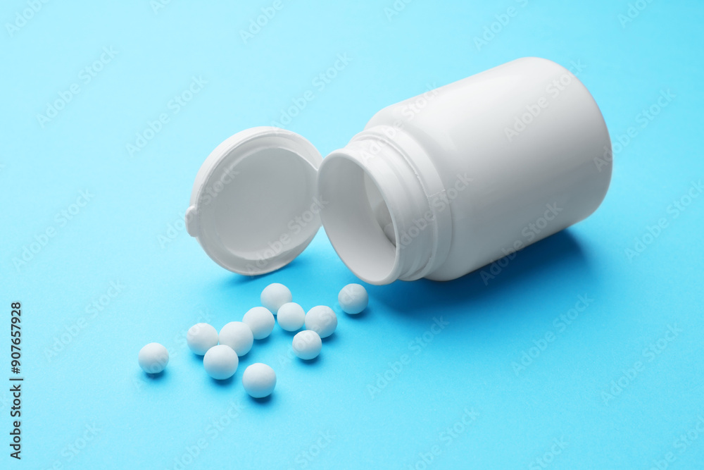 Homeopathy. Overturned plastic bottle and pills on light blue background Homeopathy. Overturned plastic bottle and pills on light blue background