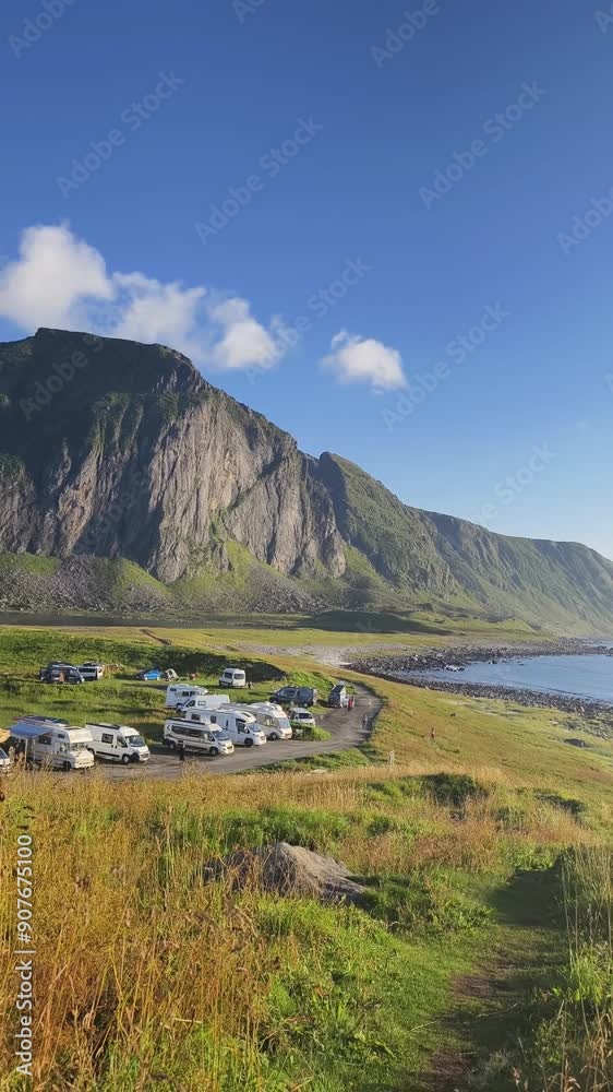 Scenic view of a campsite with caravans and tents nestled at the foot of a majestic mountain in Lofoten, Norway, under a clear blue sky Scenic view of a campsite with caravans and tents nestled at the foot of a majestic mountain in Lofoten, Norway, under a clear blue sky