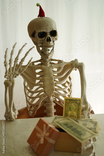 Skeleton with gift box sitting by the table .        photo