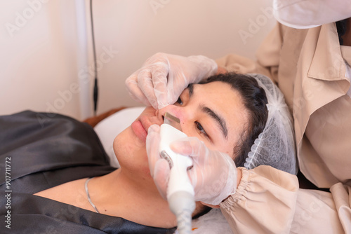 Esthetician using ultrasonic facial scrubber on male patient, scrubbing the nose area. At a esthetic clinic.