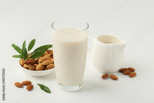 Fresh almond milk in glass, nuts, green leaves and pitcher on white background