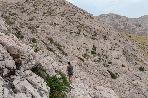 Hiker woman on scenic hiking trail to Vela Luka bay on island Otok Krk, Primorje-Gorski Kotar, Croatia. Rugged terrain in sparse vegetation. Barren landscape on Moon plateau from Hlam mountain peak photo