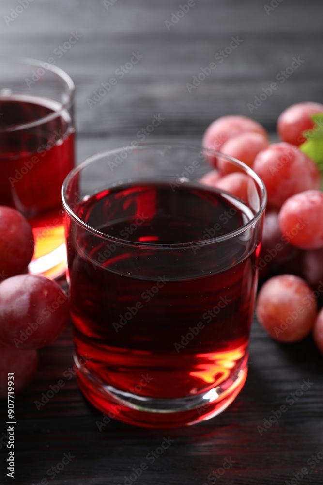 Tasty grape juice in glass and berries on black wooden table, closeup Tasty grape juice in glass and berries on black wooden table, closeup