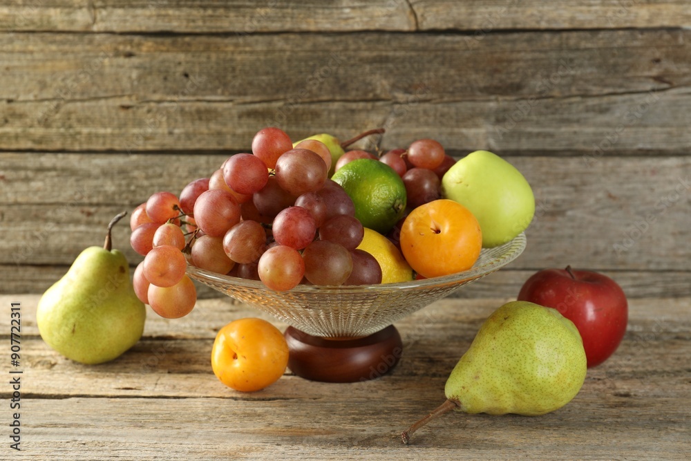 Glass vase with different fresh fruits on wooden table Glass vase with different fresh fruits on wooden table