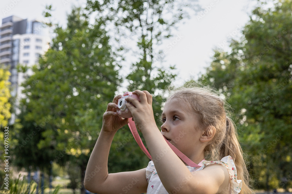 A young girl photographer takes of photo with her toy digital camera, standing in the city park. Young photographer. Hobby, photography, creativity concept A young girl photographer takes of photo with her toy digital camera, standing in the city park. Young photographer. Hobby, photography, creativity concept