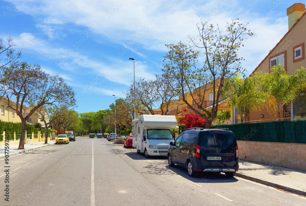 Obraz premium Campervan on parking on street near House in Spain. Family camper van vehicle at Villa. Motorhome lifestyle travel to sea. Travel on Campervan along Spain coast. Car on Parking on street in suburb.