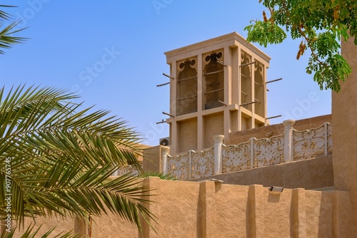 Traditional Arabic house with wind catcher tower or Barjeel for cross ventilation and passive cooling in building. Facade with palm tree, arch windows and typical middle eastern geometric ornament. 