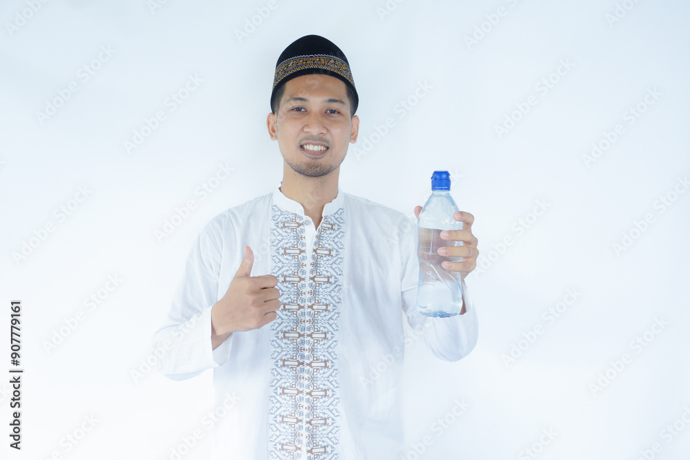 Moslem Asian man smiling at the camera while holding a bottle of drinking water Moslem Asian man smiling at the camera while holding a bottle of drinking water