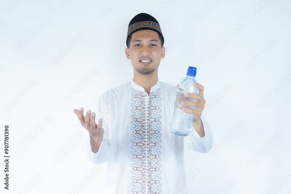 Moslem Asian man smiling at the camera while holding a bottle of drinking water Moslem Asian man smiling at the camera while holding a bottle of drinking water