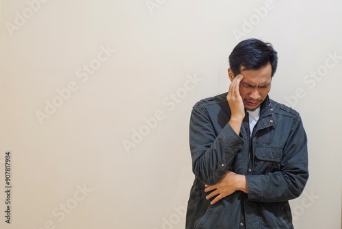 A Southeast Asian man wear brown jacket, put hand on forehead forehead, suffer from headache isolated on cream background. People lifestyle concept, Suffering migraine.