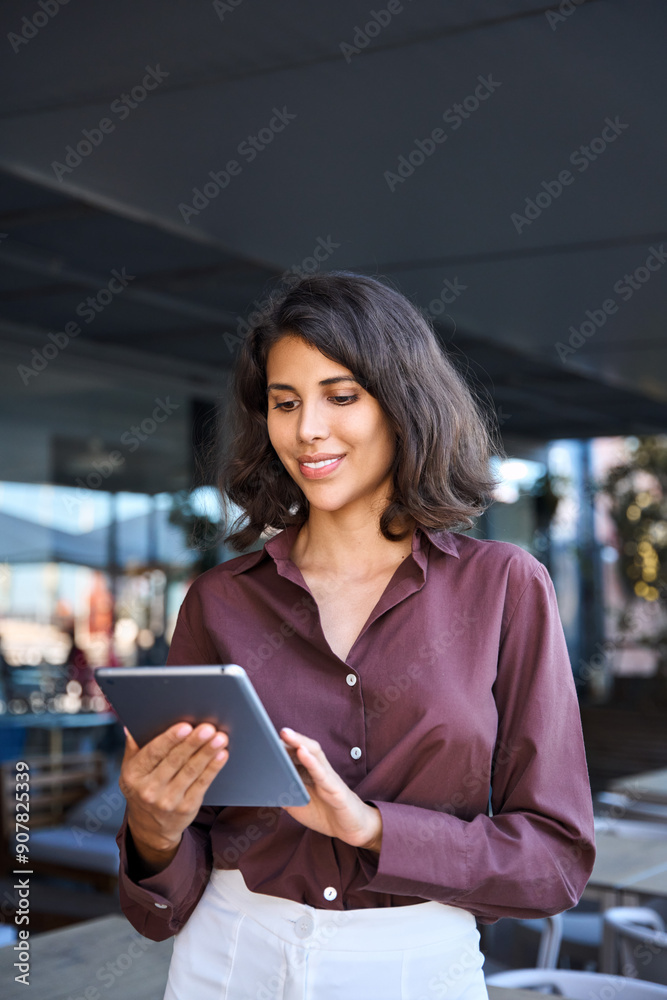 Young middle eastern businesswoman using tablet pc application for online remote work standing at office business building outdoors. Indian or latin hispanic woman holding digital computer. Vertical Young middle eastern businesswoman using tablet pc application for online remote work standing at office business building outdoors. Indian or latin hispanic woman holding digital computer. Vertical