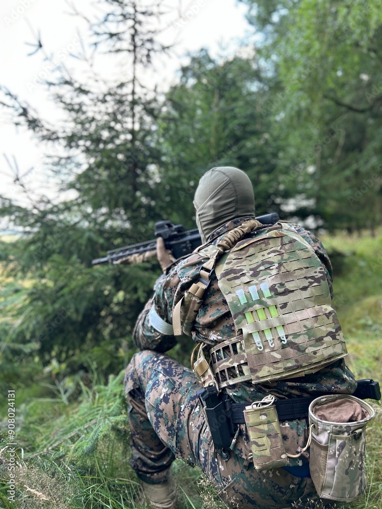 Fototapeta premium A mercenary scouts enemy territory. A soldier in camouflage with an assault rifle in his hand in the middle of the forest. Behind enemy lines. military contractor