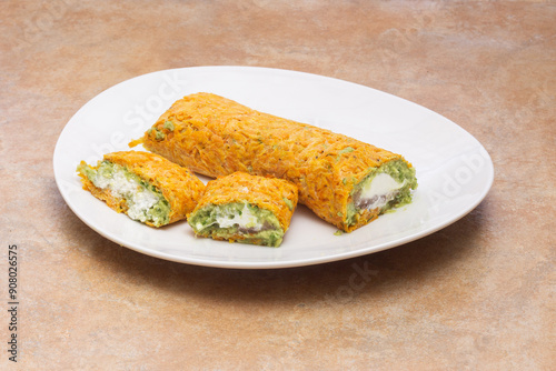 Close-up of an appetizing plate of rolled snacks with a vibrant filling of guacamole and white cheese, wrapped in an orange-hued outer layer of carrot, on a rustic countertop with copy space.